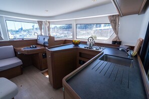 A compact galley with a sink, stove, and seating area, overlooking a marina. - Sun-Kissed Sailing Adventure in Istria, Croatia (Pula)