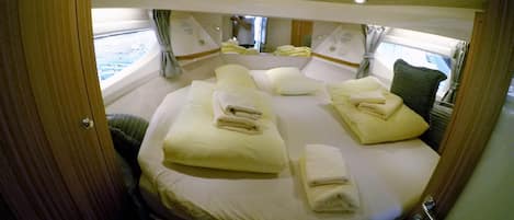 A circular bed with multiple pillows and folded towels, a window with curtains, and a wooden door.