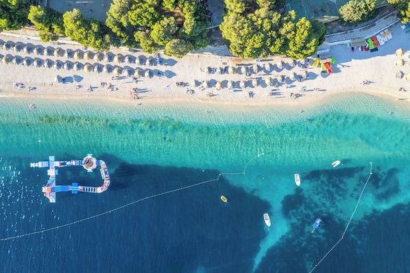 Ein Luftbild einer Strandlandschaft mit klarem türkisblauem Wasser, einem Steg und mehreren Booten.