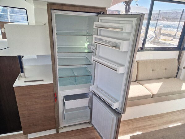 A compact refrigerator with multiple shelves and drawers, a wooden countertop, and a view of the outdoors through a window.