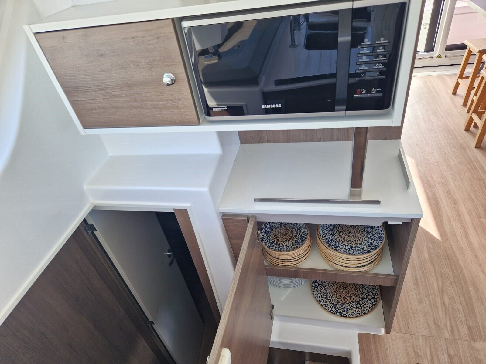 A kitchen with a microwave, a sink, and a storage area with stacked plates.
