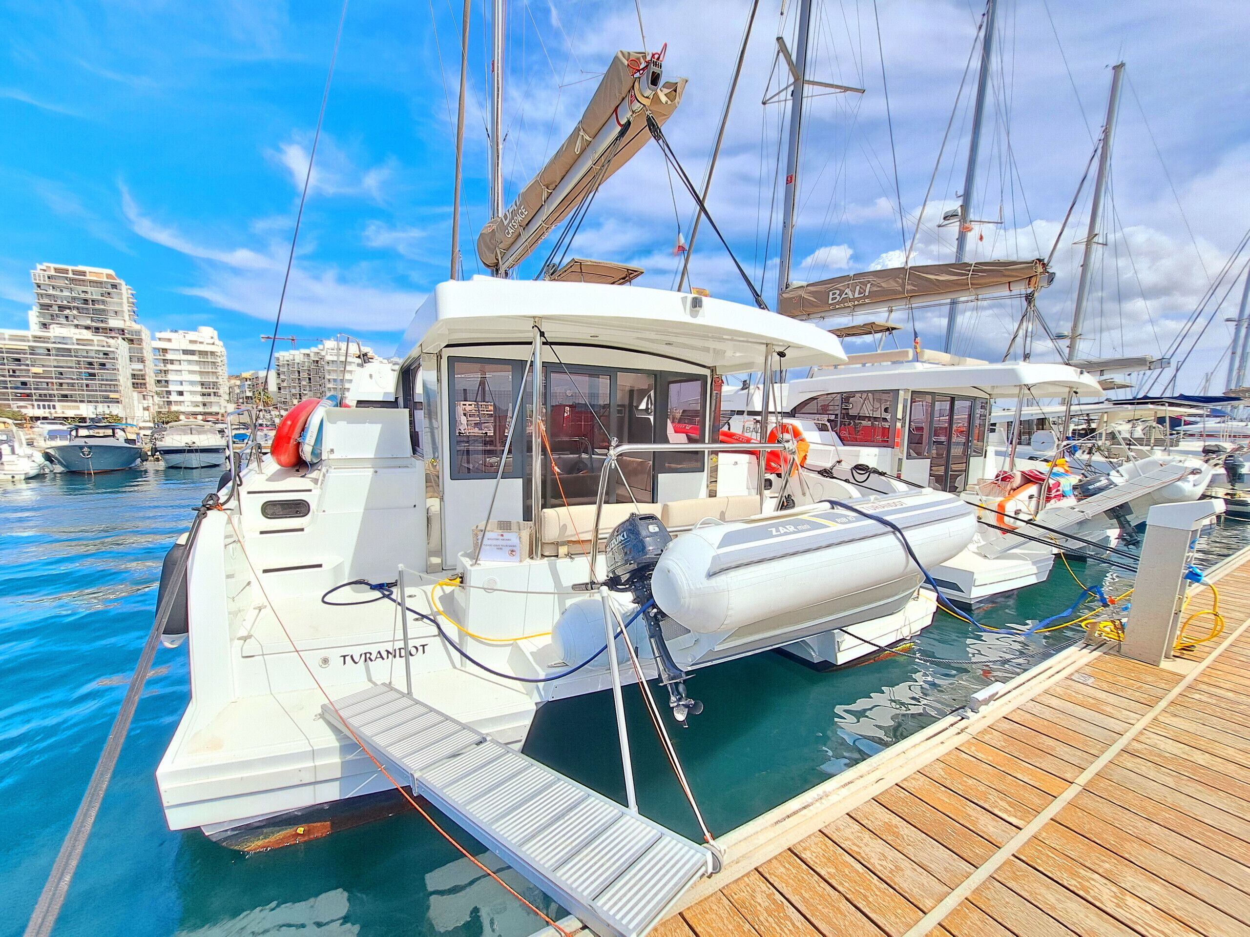 Un port de plaisance avec des bateaux amarrés, une terrasse en bois et une vue sur la ville en arrière-plan.