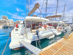 Ein Yachthafen mit vor Anker liegenden Booten, einem hölzernen Steg und einer Stadtkulisse im Hintergrund.