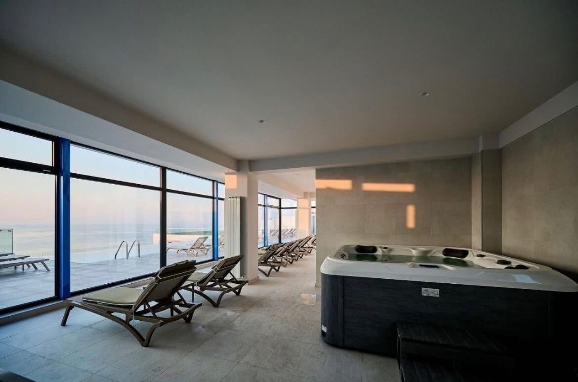 Un espace spa moderne doté d’un jacuzzi, de chaises longues et de grandes fenêtres offrant une vue panoramique.