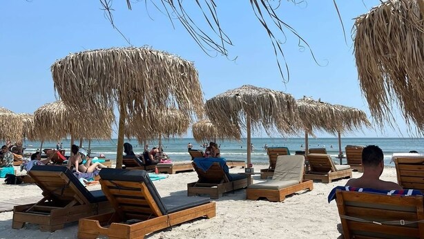 A beach with wooden lounge chairs and thatched umbrellas.