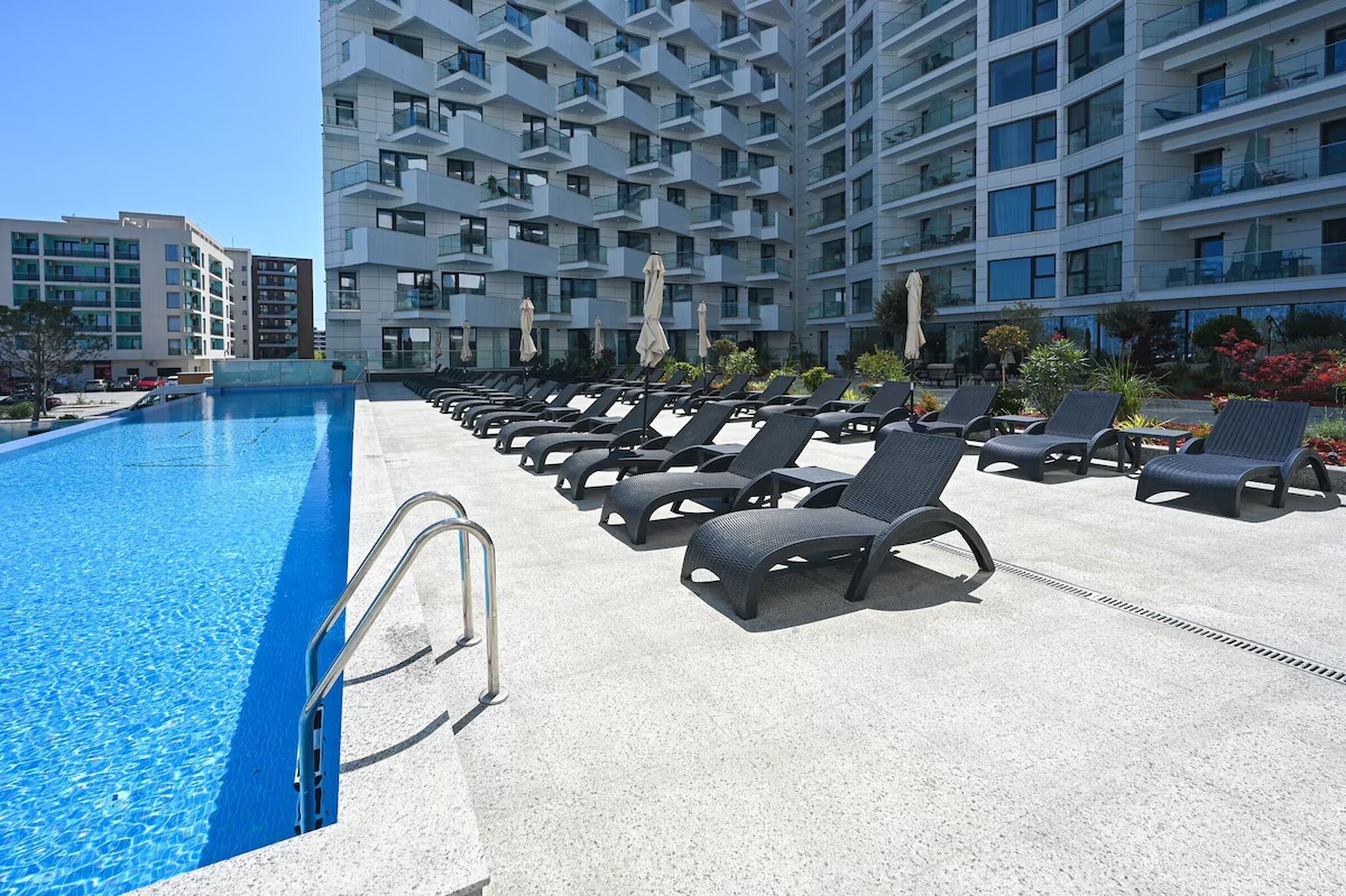 A swimming pool with lounge chairs and umbrellas, surrounded by a multi-story building with balconies.