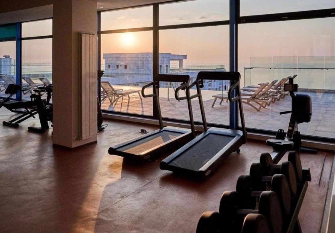 A gym with treadmills, dumbbells, and a view of the sunset through large windows.