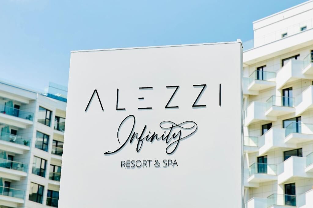 A sign for 'Alezzi Infinity Resort & Spa' with a modern building in the background.