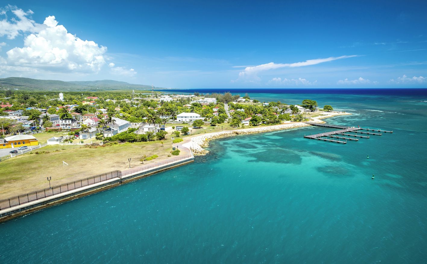 Vue aérienne d’une ville côtière avec un port de plaisance, des maisons et un phare.