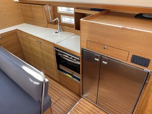 A compact kitchenette with a sink, oven, and refrigerator, wooden cabinetry, and a bench. - Sun-Kissed Sailing Adventure in Istria, Croatia (Pula)