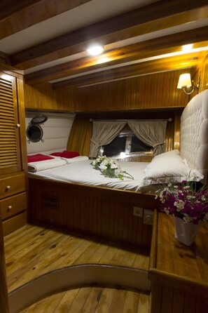 Ein gemütliches, gut beleuchtetes Kabinenzimmer mit Bett, kleinem Tisch, Topfpflanze und einem Vorhangfenster.