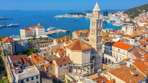 Un pueblo costero con arquitectura histórica, una torre destacada y un puerto deportivo con barcos.