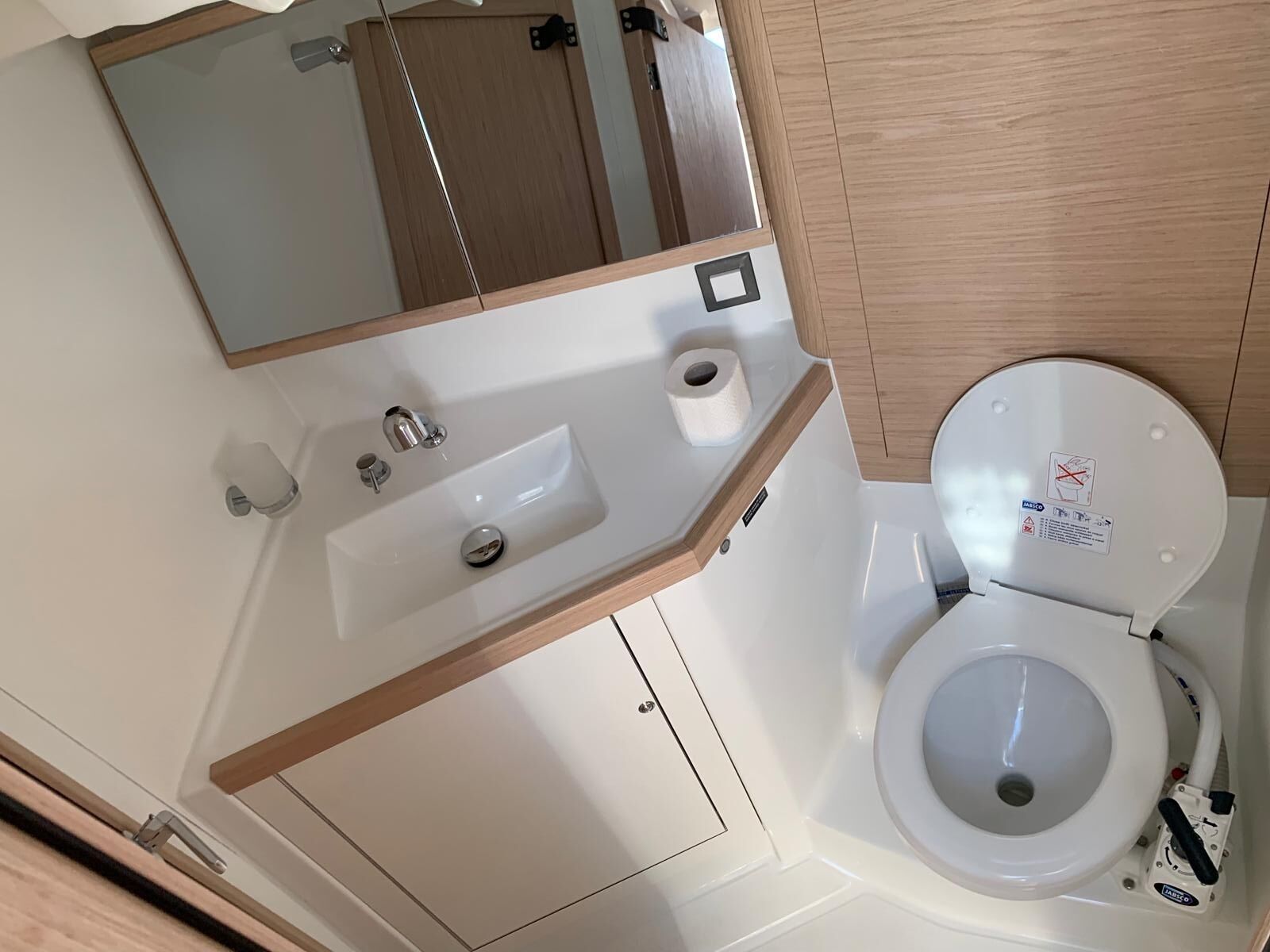 A bathroom with a sink, mirror, toilet, and wooden paneling.
