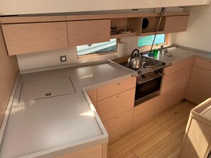 A compact kitchen with a stove, sink, and wooden cabinets. - Sun-Kissed Sailing Adventure in Zadar, Croatia (Bibinje)