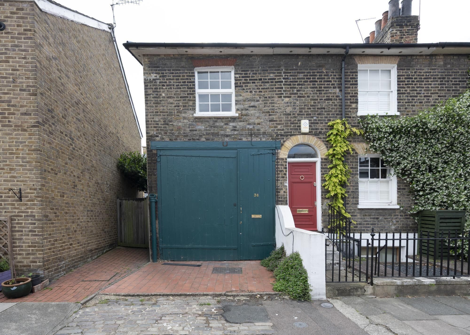 A brick house with a green gate, a red door, and a small window.