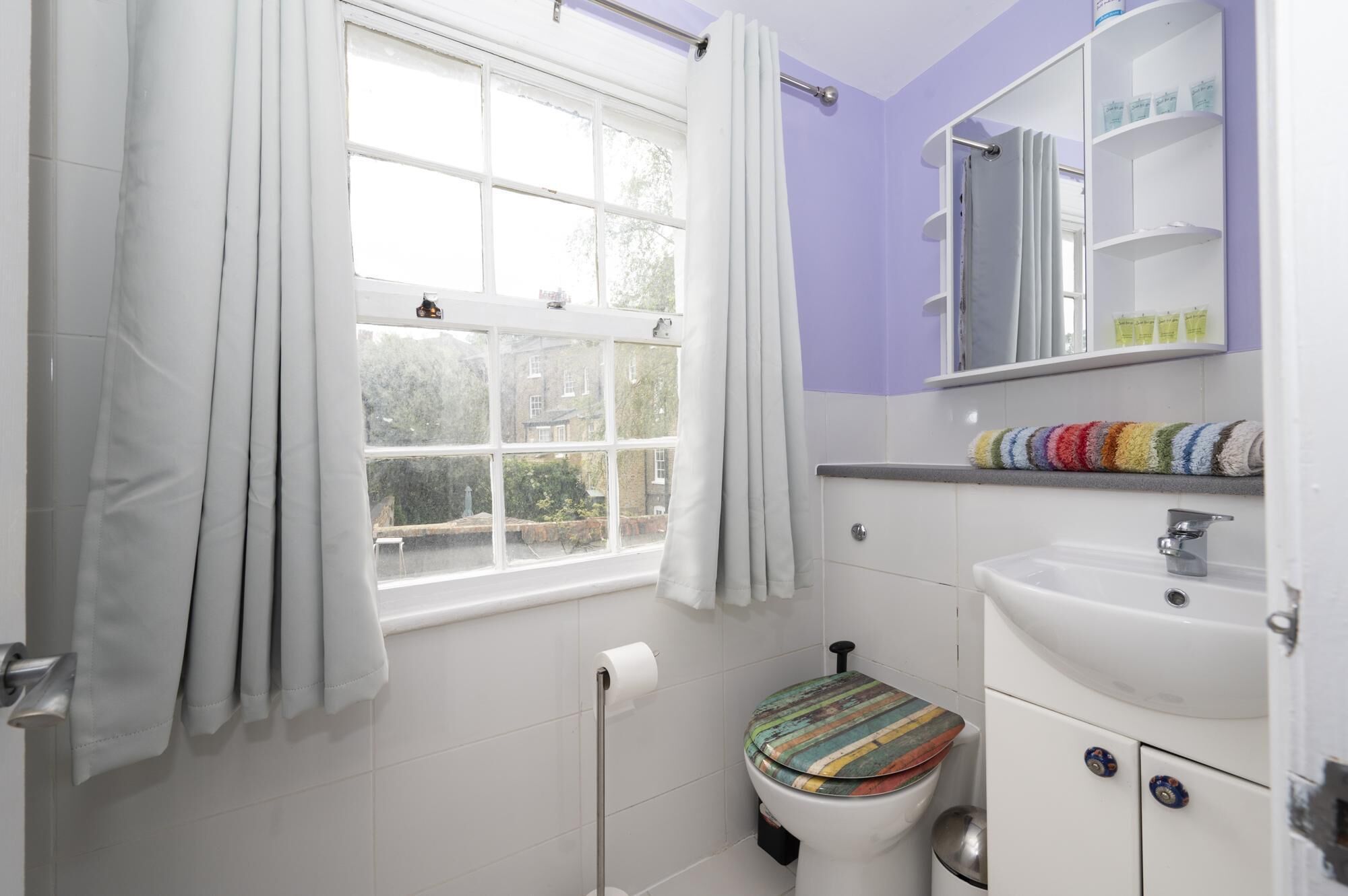 Une salle de bain avec une fenêtre, des toilettes, un lavabo et un miroir au-dessus du lavabo.