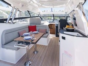 A yacht's interior with a dining area, a cushioned seating area, and a small kitchen space.
