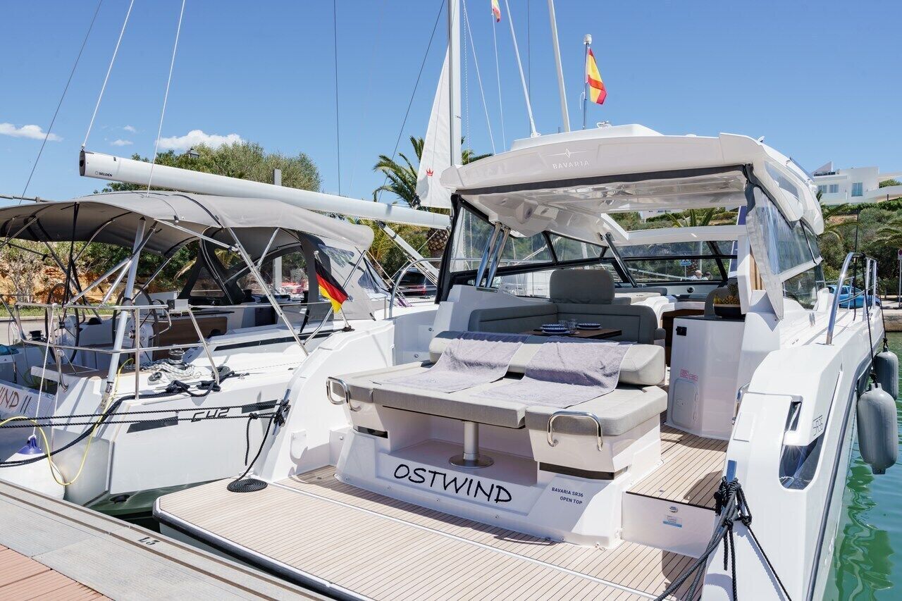 A yacht docked at a marina with a covered seating area, a name 'OSTWIND' on the deck, and a flag.
