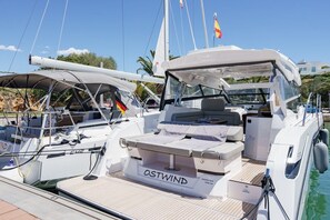 A yacht docked at a marina with a covered seating area, a name 'OSTWIND' on the deck, and a flag.