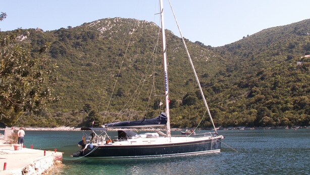 A sailboat docked at a pier with a mountainous backdrop.