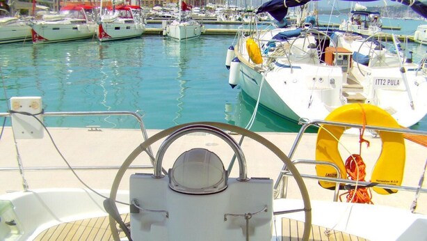 A boat's helm with a steering wheel, a life preserver, and a marina with other boats in the background. - Sun-kissed Sailing Adventure in Split-Dalmatia, Croatia (Trogir)