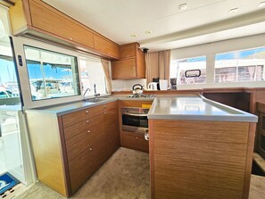 Eine kleine Küche mit Holzschränken, einer Edelstahl-Spüle und einem Fenster mit Blick auf Boote.