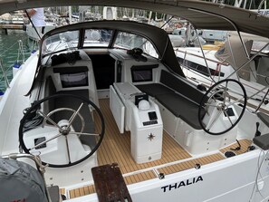 Um barco chamado THALIA com timão, painel de controle e área de assentos acolchoada.