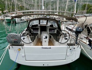 Una barca chiamata THALIA ormeggiata in una marina con diverse altre imbarcazioni, un ponte libero e un timone.