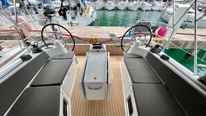 Convés de barco com assentos, timão e vista para a marina.
