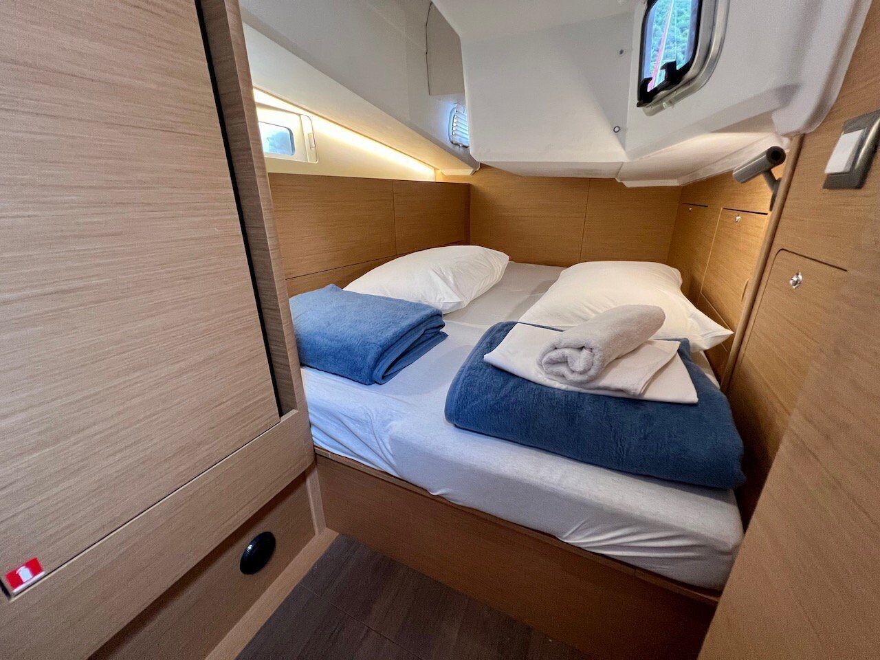 Un intérieur compact et bien éclairé, avec un lit simple, une petite fenêtre et une porte en bois.