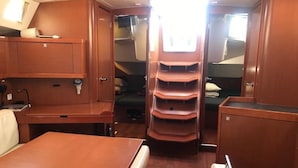 A compact cabin with a dining table, a seating area, and a central shelving unit with storage compartments. - Sun-Kissed Sailing Adventure in Islas Baleares, Mallorca (Palma)