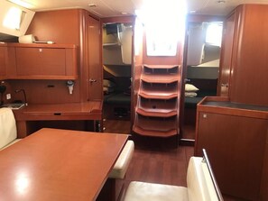 A compact cabin with a dining table, a seating area, and a central shelving unit with storage compartments. - Sun-Kissed Sailing Adventure in Islas Baleares, Mallorca (Palma)