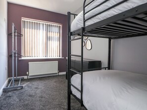 Ein Schlafraum mit Etagenbetten, einem Heizkörper, einem Fenster mit Jalousien und einem Spiegel an der Wand.
