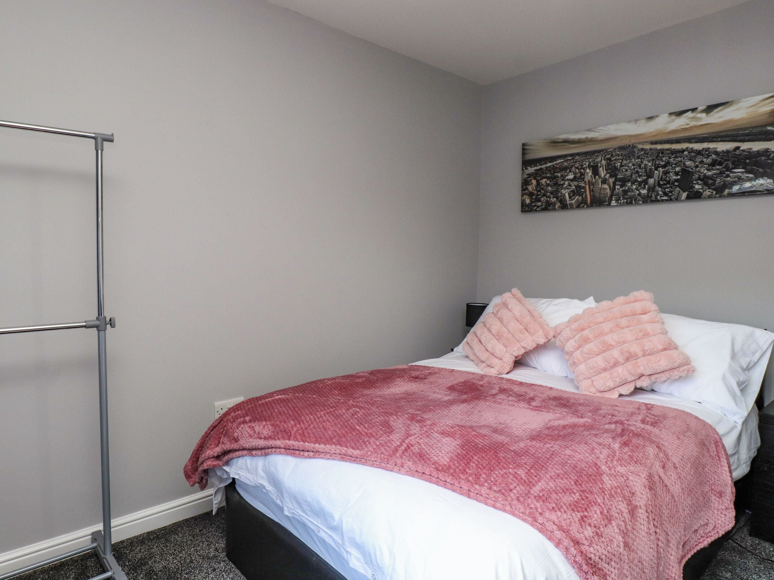 Un dormitorio con cama, pared gris, un cuadro y un atril metálico.