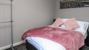A bedroom with a bed, a grey wall, a painting, and a metal stand. - Ger y Mynydd, 2 Cae Ty Coch (Brynteg)