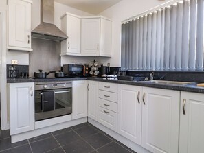 A kitchen with white cabinets, a stove, oven, and a window with curtains.