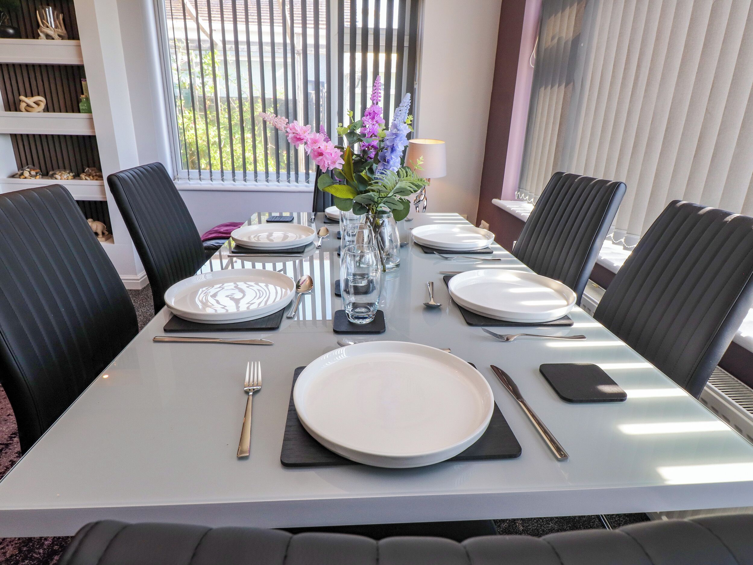A dining table set with plates, cutlery, and a vase with flowers.