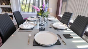 A dining table set with plates, cutlery, and a vase with flowers.