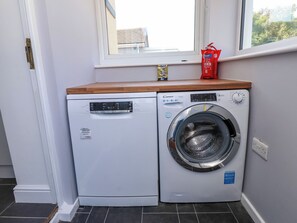 Ein kompakter Waschbereich mit einer Bosch Waschmaschine und einem Candy Trockner, ein Fenster über den Trocknern und eine kleine Ablage mit Gegenständen.