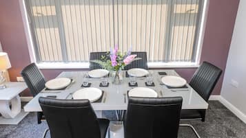 A dining area with a table set for four, chairs, a vase with flowers, and a window with blinds.