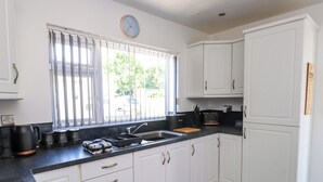 A kitchen with white cabinets, a black countertop, a sink, a coffee maker, and a clock on the wall. - Ger y Mynydd, 2 Cae Ty Coch (Brynteg)