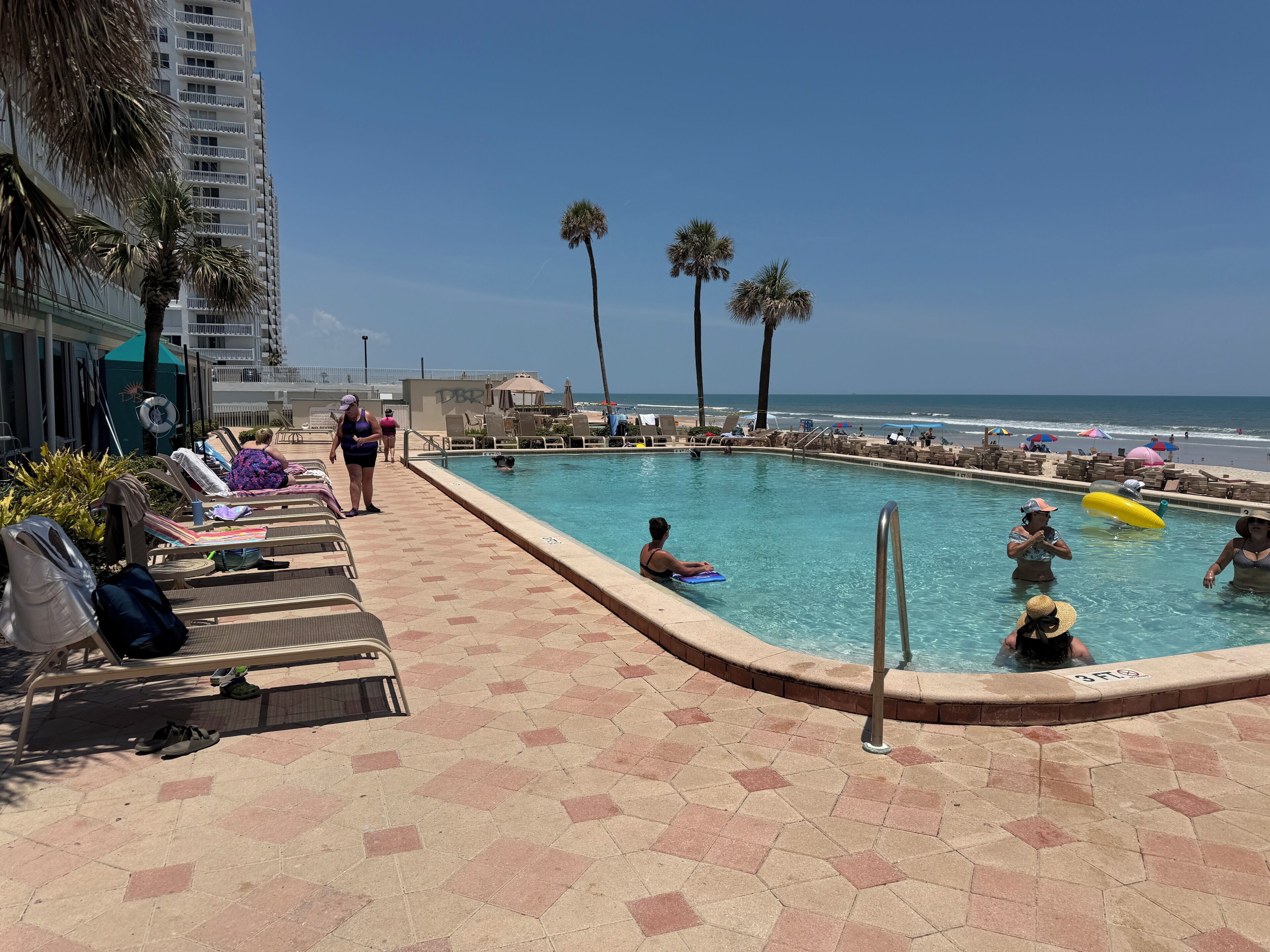 Un espace piscine comprenant des chaises longues, une piscine et une vue sur la plage.