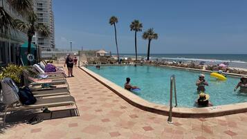 Un espace piscine comprenant des chaises longues, une piscine et une vue sur la plage.