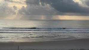 Ein Strand mit Wellen, sandigem Ufer und bewölktem Himmel.