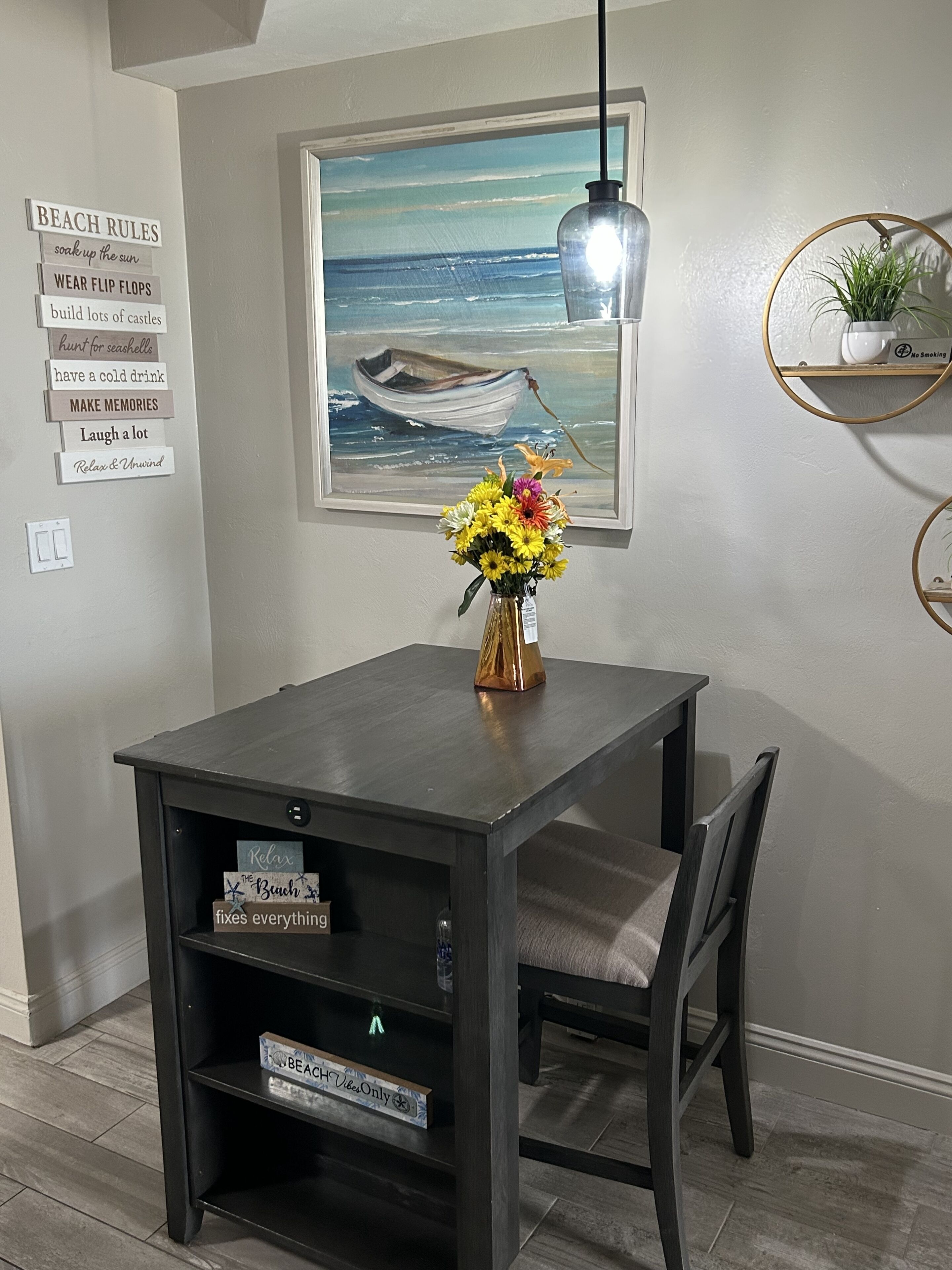 Un coin repas comprenant une table, des chaises, un vase de fleurs, un tableau représentant un bateau sur la mer et un mur orné de panneaux.
