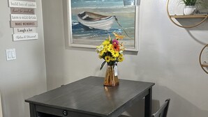 Ein Essbereich mit Tisch, Stühlen, einem Blumenstrauß, einem Gemälde von einem Boot auf See und einer Wand mit Schildern.