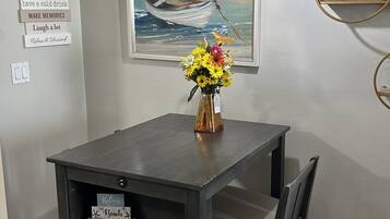 Un coin repas comprenant une table, des chaises, un vase de fleurs, un tableau représentant un bateau sur la mer et un mur orné de panneaux.