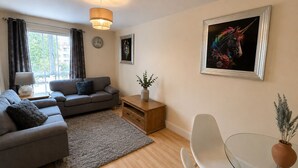 Ein modernes Wohnzimmer mit einem grauen Sofa, einem kleinen Tisch mit einer Vase, einem weißen Stuhl und einem Gemälde an der Wand.