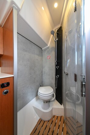 Une petite salle de bain comprenant des toilettes, une douche et un meuble-lavabo en bois.