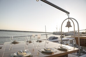 A table set for a meal with glasses and plates, a bell, and a view of the water. - Sun-Kissed Sailing Adventure in Islas Sarónicas (Alimos)